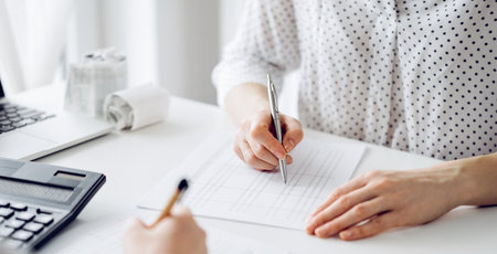 Two accountants using a laptop computer and calculator for counting taxes at white desk in office. Teamwork in business audit and financeの写真素材