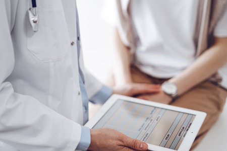 Doctor and patient discussing health exam results. Friendly physician reassuring a young woman by one hand while keeping tablet computer in another. Medicine conceptの写真素材
