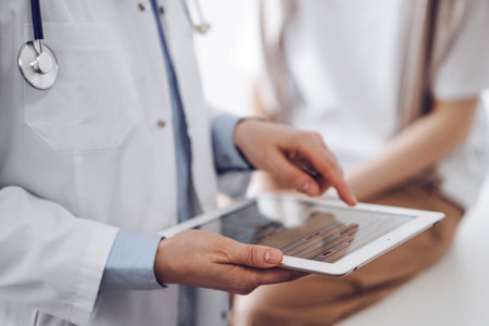 Doctor and patient in clinic. Friendly physician using tablet computer near a young woman. Medicine conceptの写真素材