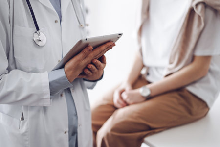 Doctor and patient discussing perfect health exam results. Friendly physician keeping tablet computer with her hands near a young woman. Medicine conceptの写真素材