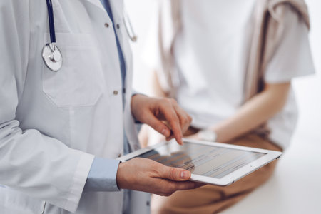 Doctor and patient in clinic. Friendly physician using tablet computer near a young woman. Medicine conceptの写真素材