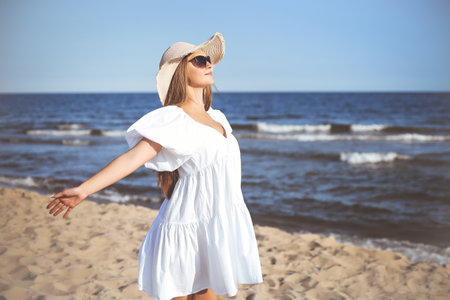 Happy blonde woman is on the ocean beach in a white dress and sunglasses, open armsの写真素材