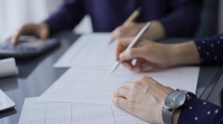 Two unrecognizable female accountants or auditors are sitting and reviewing financial documents in office. Audit and taxesの写真素材
