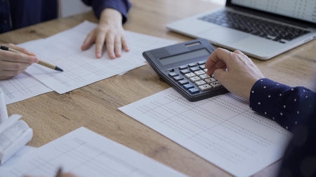 Accountants or auditors reviewing financial documents while using laptop, calculator and sitting...