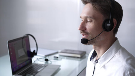Businessman wearing headset and glasses, using laptop for video conference call, working remotely...