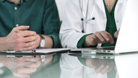 Doctor woman is typing on laptop computer while listening to patient complaints during medical consultation in clinic office. Medicine conceptの写真素材