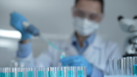 Laboratory tubes are in focus, closeup view. Female scientist researcher is using a micropipette at...