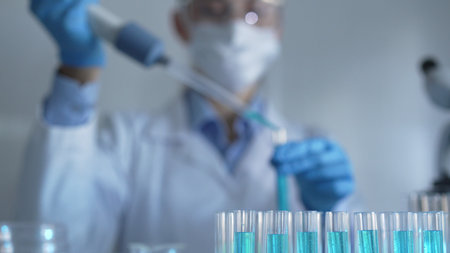 Test tubes with a blue liquid are in focus in laboratory setting, closeup view. Female scientist...