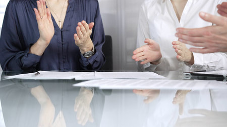 Unrecognizable business professionals applauding and celebrating achievements at glass table after successful meeting. Business people concept, close up viewの写真素材