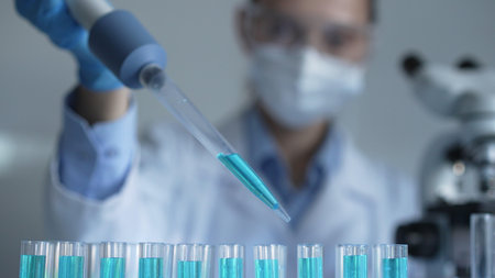 Close up of a female scientist researcher hand using a micropipette to fill up test tubes with a blue liquid in laboratory. Medicine and scienceの写真素材