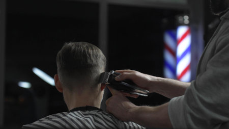 Skilled barber trimming clients hair with electric razor, creating precise contemporary hairstyle inside sleek urban barbershop settingの写真素材