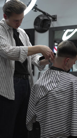 Professional barber grooming clients hair using electric clipper, delivering precise cut with skill in contemporary salon settingの写真素材
