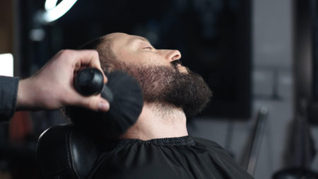 Skilled barber brushing clients beard, providing precise grooming within elegant barbershop setting, highlighting professional hair styling expertiseの写真素材