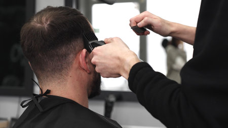 Skilled barber trimming clients hair using electric razor, creating contemporary hairstyle in modern barbershop setting with precise, professional techniqueの写真素材