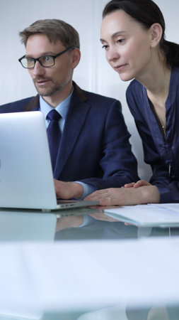 Two professionals collaborating in a modern office setting, using a laptop and discussing a project, vertical portrait. Business people conceptの写真素材