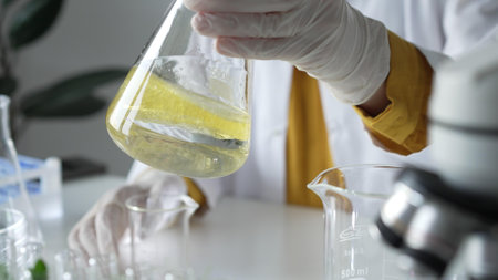 Unknown scientist wearing white protective gloves is carefully shaking up a yellow chemical solution inside an Erlenmeyer flask in a laboratory, close up. Science and medicineの写真素材