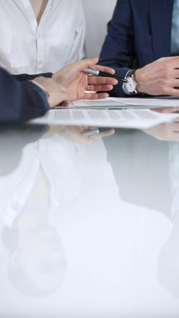 Unrecognizable business people are reviewing contract terms during a meeting while sitting at the glass table in office, vertical close up view. Copy space areaの写真素材