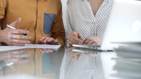 Two accountants are discussing a tax audit, using a laptop and reviewing documents at a glass table. Taxes, audit in businessの写真素材