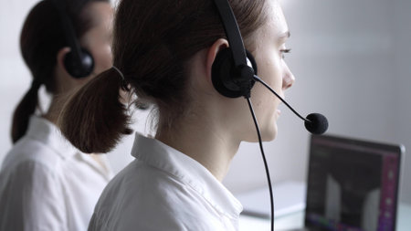 Young female call center operator in white blouse is assisting clients online, providing customer support and answering inquiries. Business call centerの写真素材