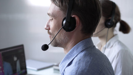 Happy smiling male call center operator in blue casual shirt is assisting clients online, providing customer support and answering inquiries. Business call centerの写真素材
