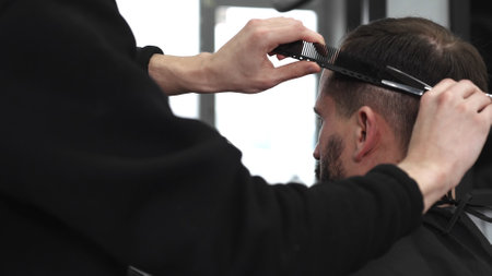 Skilled barber trimming clients hair using professional scissors, creating precise hairstyle in contemporary salon with modern interior and relaxed atmosphereの写真素材