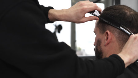 Skilled barber trimming clients hair using professional scissors, creating precise hairstyle in contemporary salon with modern interior and relaxed atmosphereの写真素材
