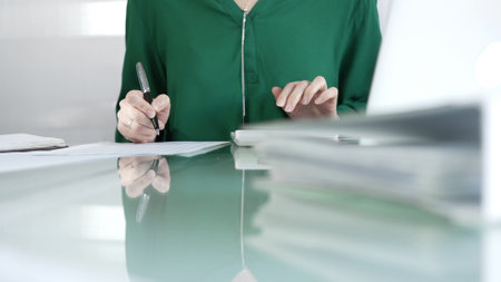 Businesswoman accountant at a sleek glass desk in a contemporary office, using a calculator to crunch numbers and jotting down meticulous notes, green color style. Taxes, audit in businessの写真素材
