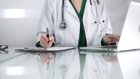 Woman doctor using a clipboard and taking notes on glass desk in a medical office, close-up view. Medicine conceptの写真素材