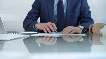 Businessman pointing at charts with pen, explaining data to colleague while sitting at the glass table in office. Businesspeople conceptの写真素材