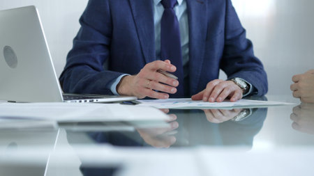 Businessman pointing at charts with pen, explaining data to colleague while sitting at the glass table in office. Businesspeople conceptの写真素材
