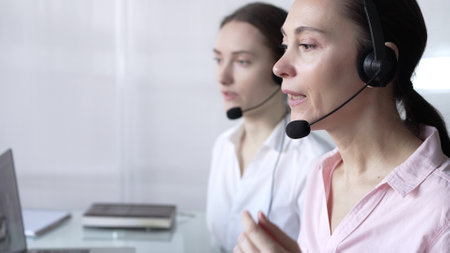 Focused female call center operator in pink casual blouse is assisting clients online, providing customer support and answering inquiries. Business call centerの写真素材