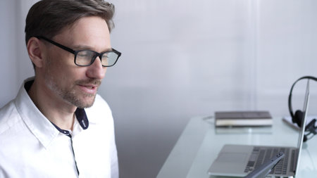 Businessman office worker attending online meeting using laptop and microphone, working remotely from home or office. Businesspeople conceptの写真素材