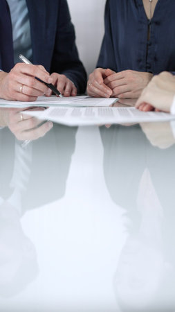 Unrecognizable business people are discussing a contract during meeting while sitting at the glass table in office, vertical close up view. Copy space areaの写真素材