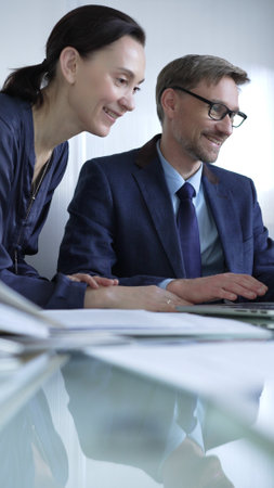 Two professionals collaborating in a modern office setting, using a laptop and discussing a project, vertical portrait. Business people conceptの写真素材