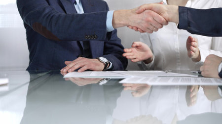 Unrecognizable business partners shaking hands after signing contract at glass table in office meeting, making a deal and closing agreement, close up of handshakeの写真素材
