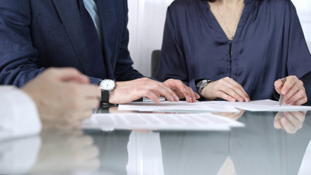 Business people reviewing contract terms while sitting at the glass desk during a meeting, negotiation in office, close up view. Success conceptの写真素材