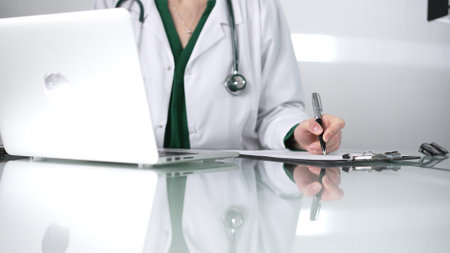 Woman doctor using a clipboard and taking notes on glass desk in a medical office, close-up view. Medicine conceptの写真素材