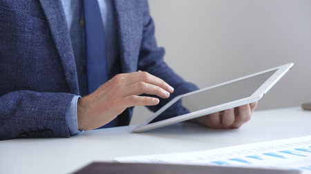 Businessman is using a digital tablet to analyze financial data, working with modern technology in...