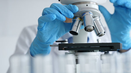 Close up of scientists gloved hands adjusting microscope, conducting research in laboratory with...
