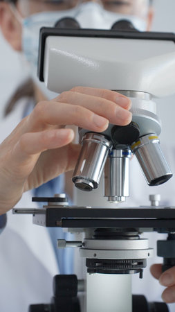 Female scientist wearing lab coat and protective glasses using a modern microscope in a laboratory...