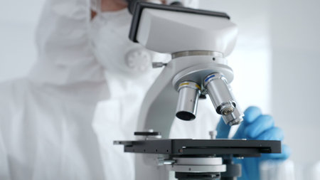 Close up of scientific researcher or virologist wearing protective gear is adjusting microscope,...