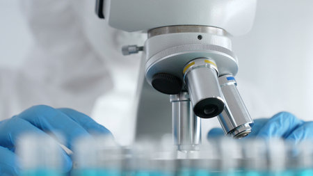 Scientific researcher or virologist wearing protective gear is tuning microscope lenses opposite the...