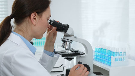 Female scientist examining microscope slide, analyzing blue chemical sample in sterile laboratory...