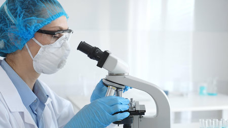 Female researcher examining sample through microscope, conducting medical experiment inside sterile...
