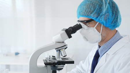 Experienced scientist examining microscopic sample, wearing full protective gear inside sterile...