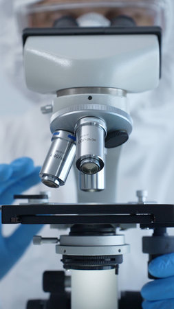 Medical virologist in a hazmat suit, mask, and gloves, diligently working at a microscope in a...