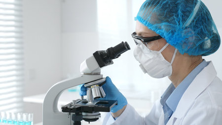 Female researcher examining sample through microscope, conducting medical experiment inside sterile...