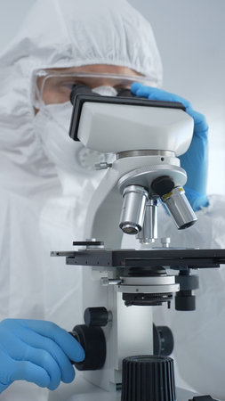 Male scientist virologist wearing hazmat suit, mask, and blue gloves, diligently working at a...