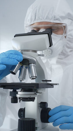 Male scientist virologist wearing hazmat suit, mask, and blue gloves, diligently working at a...