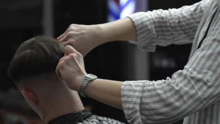 Skilled barber trimming customers hair using professional scissors and comb, working in contemporary...